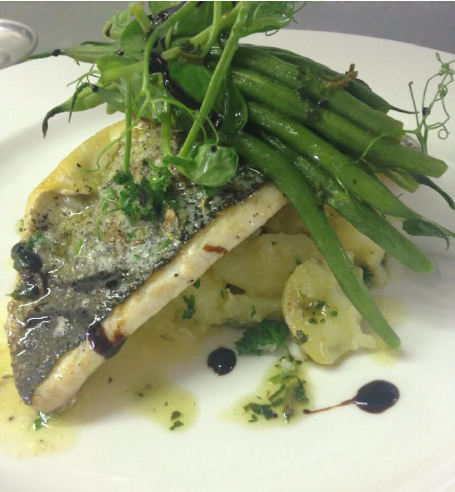 A fillet of pan fried sea bass with crushed potatoes, green beans and pea shoots